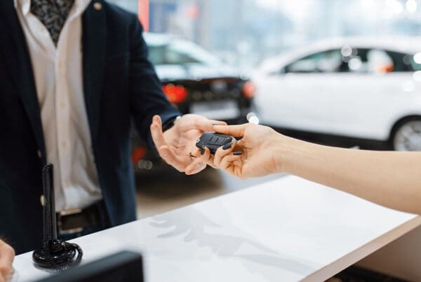 Should I Purchase Rental Car Insurance? - Man Takes the Key From New Auto in Car Dealership as the Appers Are Being Signed a the Sun is Shining on the New Cars