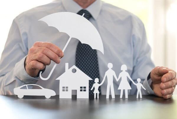 What is an Umbrella Insurance Policy? - Family, Home and Car Protection Under a Cut Out of an Umbrella Held by a Man in a Suit in the Kitchen