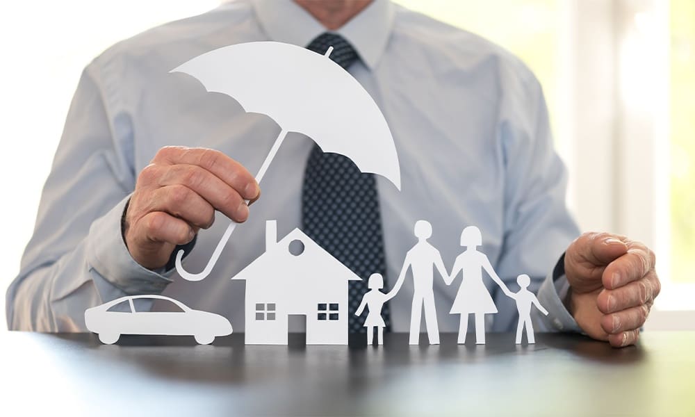 What is an Umbrella Insurance Policy? - Family, Home and Car Protection Under a Cut Out of an Umbrella Held by a Man in a Suit in the Kitchen